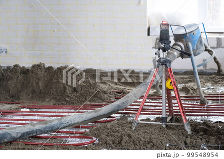 Semi-dry floor screed - a worker shovels a construction mixture through a special sleeve for cementing and leveling on underfloor heating pipes. 99548954