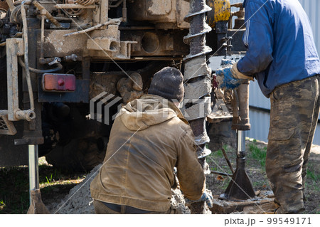 Team of workers with drilling rig on car are drilling artesian well for water in ground. Insertion of metal casing pipe into ground, installation of individual drinking supply, June 28, 2022, Russia, 99549171