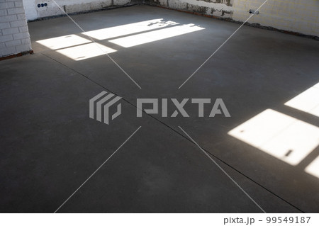 The leveled rough floor in a house under construction with a semi-dry cement screed is a smooth surface with light from the windows 99549187