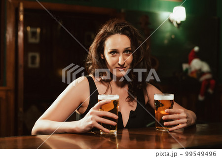 sexy woman with big breasts with two glasses of lager beer in hand at bar 99549496