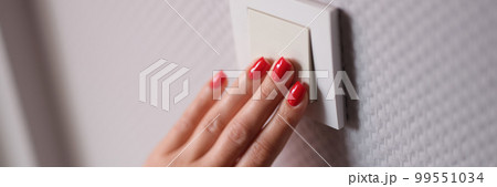 Female hand presses white switch on gray wall closeup Female hand presses white switch on gray wall closeup 99551034
