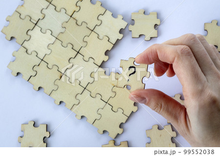 Woman's hand holds a wooden puzzle with a question mark against a background of empty puzzles. The concept of problem solving. 99552038