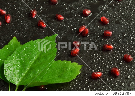 Closeup juicy fresh pomegranate arils with green leaf on black 99552787