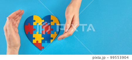 Father and autistic son hands holding jigsaw puzzle heart shape. World Autism Awareness Day 99553904