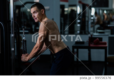Shirtless man doing triceps pulldown at the gym.  99556376