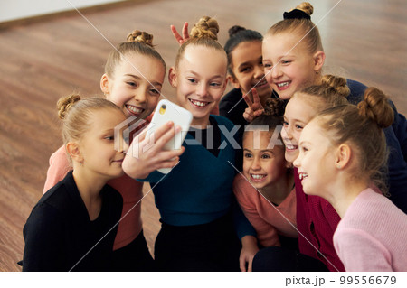 Group of beautiful little girls, children, rhythmic gymnasts doing selfie with phone after training session indoors. Friendly team. Concept of sport, childhood, rhythmic gymnastics 99556679