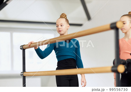 Beautiful little girls, children, gymnasts training indoors. Stretching exercises with barre equipment. Concept of sport, childhood, rhythmic gymnastics Beautiful little girls, children, gymnasts training indoors. Stretching exercises with barre equipment. Concept of sport, childhood, rhythmic gymnastics 99556730