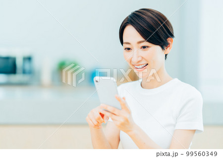 キッチンでスマートフォンを操作するミドル女性。 キッチンでスマートフォンを操作するミドル女性。 99560349