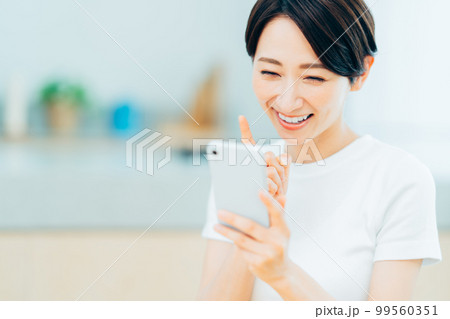 キッチンでスマートフォンを操作するミドル女性。 99560351