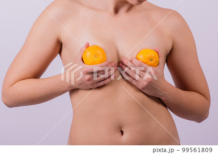 Slender athletic woman topless holds a tangerine in her hands. Cellulite. Healthy lifestyle Slender athletic woman topless holds a tangerine in her hands. Cellulite. Healthy lifestyle 99561809
