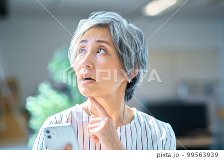 オフィスでスマホを操作するシニアビジネスウーマン オフィスでスマホを操作するシニアビジネスウーマン 99563939