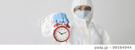Person in protective suit with glasses and mask holds alarm clock 99564944