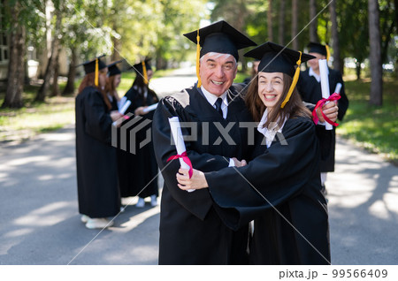 A group of graduates in robes outdoors. An elderly man and a young woman congratulate each other on their graduation. A group of graduates in robes outdoors. An elderly man and a young woman congratulate each other on their graduation. 99566409
