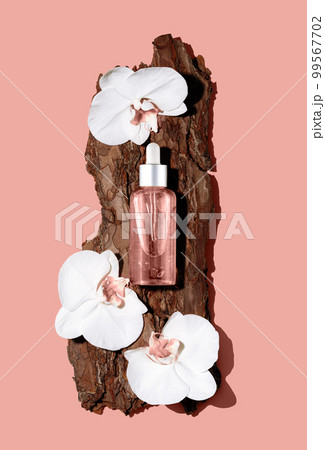 Glass cosmetic bottle on textured tree bark podium with white orchid flowers on pastel pink background. Demonstration of cosmetic product with copy space in flat lay style. Glass cosmetic bottle on textured tree bark podium with white orchid flowers on pastel pink background. Demonstration of cosmetic product with copy space in flat lay style. 99567702