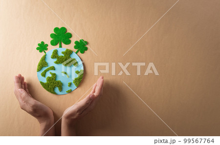 Hands holding paper earth with grass on brown background. World environment day, earth day and save earth concept. Hands holding paper earth with grass on brown background. World environment day, earth day and save earth concept. 99567764