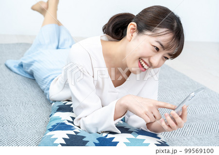 寝転んでスマホを使う女性 寝転んでスマホを使う女性 99569100
