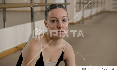 Tired ballerina in dance studio looks at camera Tired ballerina in dance studio looks at camera 99572118