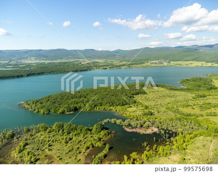 Aerial view on mountain lake. Drone over water reservoir at mountain valley covered with green spring forest. Beautiful view from above on smooth blue surface of mountain lake among highlands. Nobody Aerial view on mountain lake. Drone over water reservoir at mountain valley covered with green spring forest. Beautiful view from above on smooth blue surface of mountain lake among highlands. Nobody 99575698