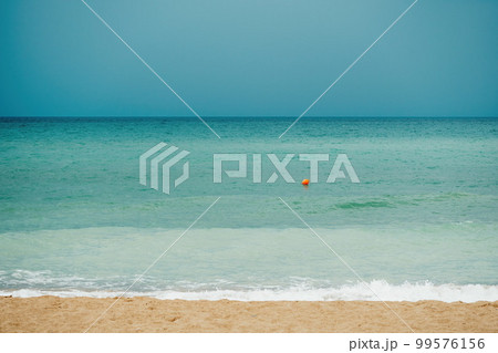 Overcast sky on rainy day with foamy waves rolling towards golden sand beach under low warm sun light. Nobody. Holiday recreation concept. Abstract nautical summer ocean sunset nature. 99576156