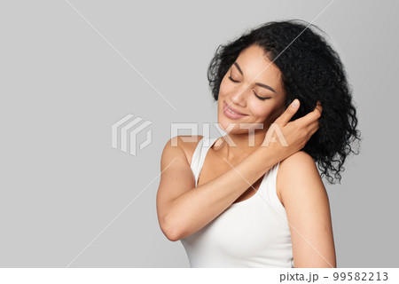 Nice cheerful mixed race girl with closed eyes touching her hair 99582213