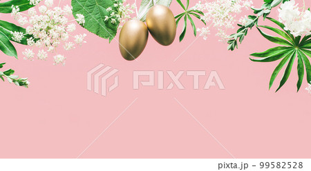 Golden Easter eggs in assorted floral and jungle tree green leaves and white flowers corner border on peach pink. Natural sustainable environment friendly cosmetics mockup flat lay banner 99582528