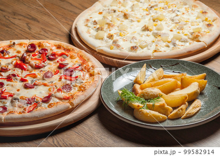 Two different pizzas on the boards and fried potatoes in a plate on the table Two different pizzas on the boards and fried potatoes in a plate on the table 99582914