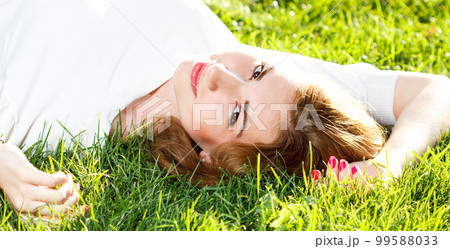 Beautiful smiling woman lying on a grass outdoor. She is absolutely happy.  99588033