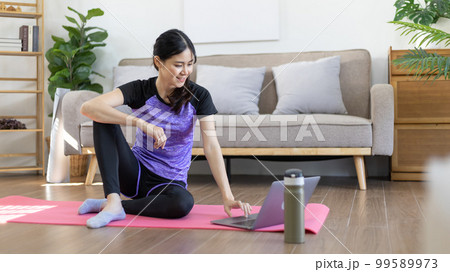 Woman looking at yoga teacher on laptop and doing light exercise in the living room at home, Watch live teaching or VDO on laptop, Dumbbells and a protein shake or bottle of water, Healthy exercise. Woman looking at yoga teacher on laptop and doing light exercise in the living room at home, Watch live teaching or VDO on laptop, Dumbbells and a protein shake or bottle of water, Healthy exercise. 99589973