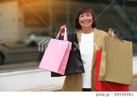Black friday. Smiling adult woman with shopping bags. Middle ages female after shopping on shopping mall background. Purchases, discounts, sale concept. Online shopping concept, Seasonal Sales. mockup Black friday. Smiling adult woman with shopping bags. Middle ages female after shopping on shopping mall background. Purchases, discounts, sale concept. Online shopping concept, Seasonal Sales. mockup 99590461