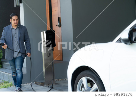 Progressive asian man recharge his EV car at home charging station. Progressive asian man recharge his EV car at home charging station. 99591276