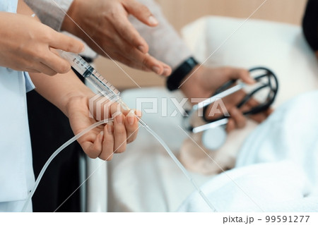 Doctor and nurse inject medicine, dosage into IV tube in sterile recovery room 99591277