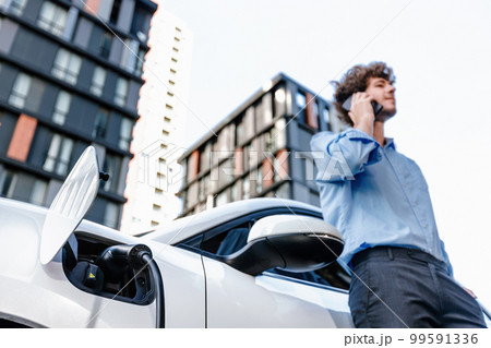 Progressive businessman talking on the phone with recharging electric vehicle. Progressive businessman talking on the phone with recharging electric vehicle. 99591336