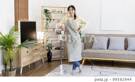Beautiful housewife standing next to a vacuum cleaner and ready to do a big house cleaning job, Big cleaning in the house, Removes germs and dirt and deep stains, Housewife cleaning, Domestic hygiene. 99592944