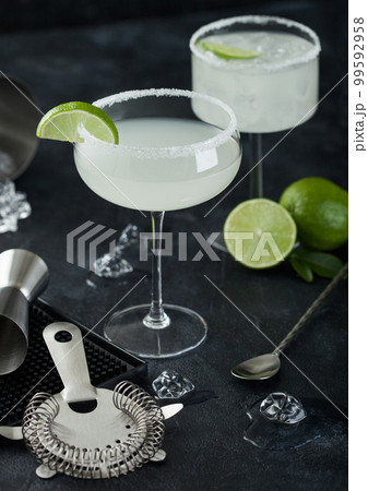 Luxury glasses of Margarita cocktail with fresh limes and bar mat with strainer and jigger Luxury glasses of Margarita cocktail with fresh limes and bar mat with strainer and jigger 99592958