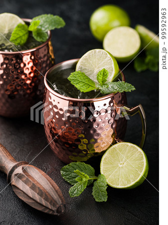 Moscow mule cocktail in a copper mug with lime and mint and wooden squeezer on dark kitchen Moscow mule cocktail in a copper mug with lime and mint and wooden squeezer on dark kitchen 99592963
