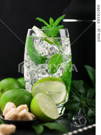 Glass of Mojito cocktail with ice cubes mint and lime on black board with spoon and fresh limes Glass of Mojito cocktail with ice cubes mint and lime on black board with spoon and fresh limes 99592966