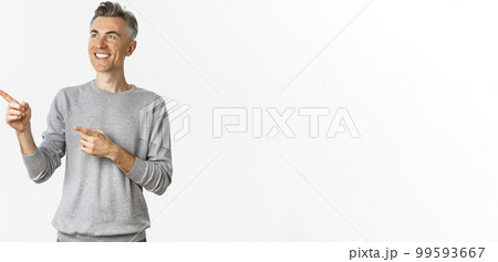 Image of smiling handsome middle-aged man looking at logo, pointing fingers left and showing advertisement, standing over white background 99593667