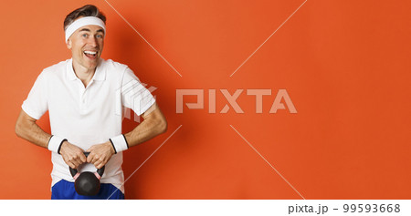 Concept of workout, gym and lifestyle. Image of handsome middle-aged guy doing sport exercises, lifting kettlebell and smiling, standing over orange background 99593668