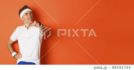 Concept of sport, fitness and lifestyle. Portrait of confident, healthy middle-aged sportsman, pointing finger at camera and smiling, need you, standing over orange background Concept of sport, fitness and lifestyle. Portrait of confident, healthy middle-aged sportsman, pointing finger at camera and smiling, need you, standing over orange background 99593744