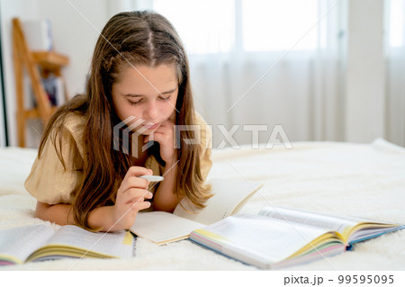 Caucasian girl lie on bed and concentrate with reading and do the homework in bedroom 99595095