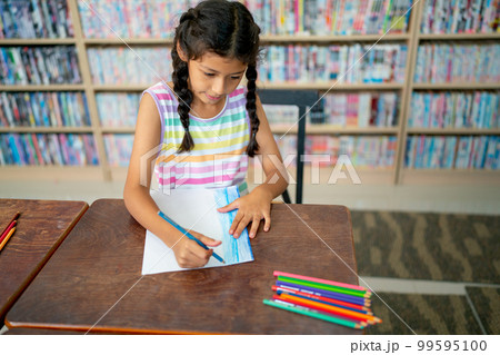 Little Asian girl enjoy to paint the picture using colored pencils in classroom at school. 99595100