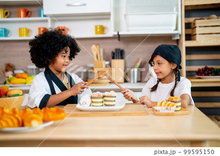 Two little girls, African American and Asian girls use wooden spoon and fork to play and fun 99595150