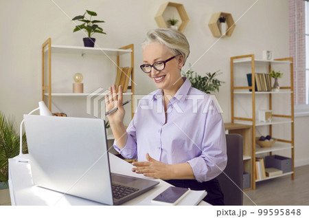 An elderly gray-haired woman with a smile on her face uses a laptop to communicate. An elderly gray-haired woman with a smile on her face uses a laptop to communicate. 99595848