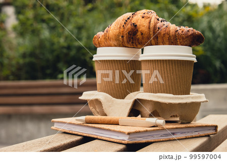 Fresh baked chocolate croissant on Two paper cups with lid for tea to go. Empty paper notebook. Freelancer's place of work. Study and work online. Remote business education. Making plans for next week Fresh baked chocolate croissant on Two paper cups with lid for tea to go. Empty paper notebook. Freelancer's place of work. Study and work online. Remote business education. Making plans for next week 99597004