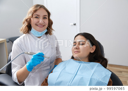 Dentist drilling tooth of female patient in dental chair 99597065