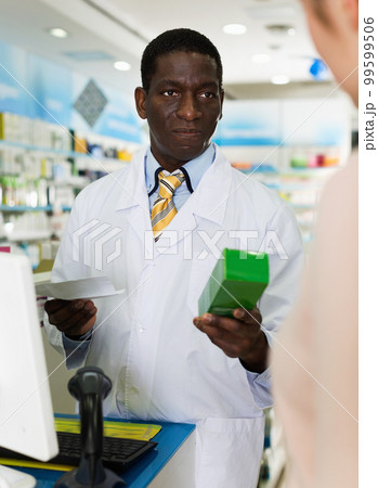 African American man pharmacist handing prescribed medicine to customer in pharmacy 99599506