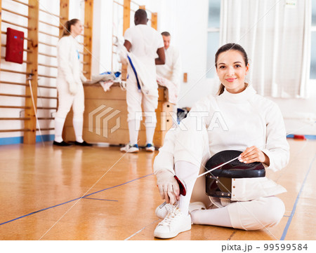 Woman in uniform sitting on floor at fencing training 99599584