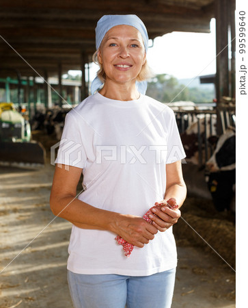 Smiling mature female proffesional farmer standing near cows Smiling mature female proffesional farmer standing near cows 99599640