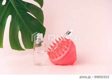 Massager for scalp and cosmetics against pink background and monstera leaf Massager for scalp and cosmetics against pink background and monstera leaf 99602932