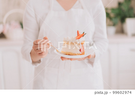 Confectioner in white uniform holding cut piece of mousse cake with strawberries Confectioner in white uniform holding cut piece of mousse cake with strawberries 99602974